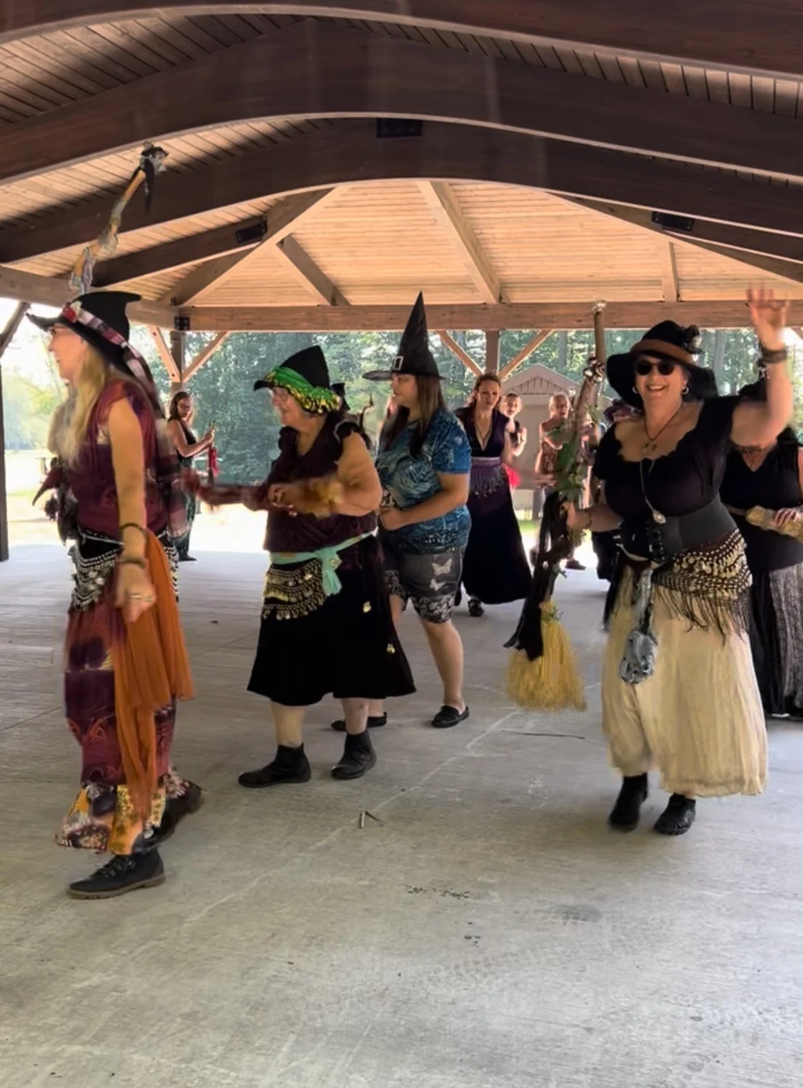 A group of women dressed as witches dance under a park pavilion at CNY Pagan Pride Day
