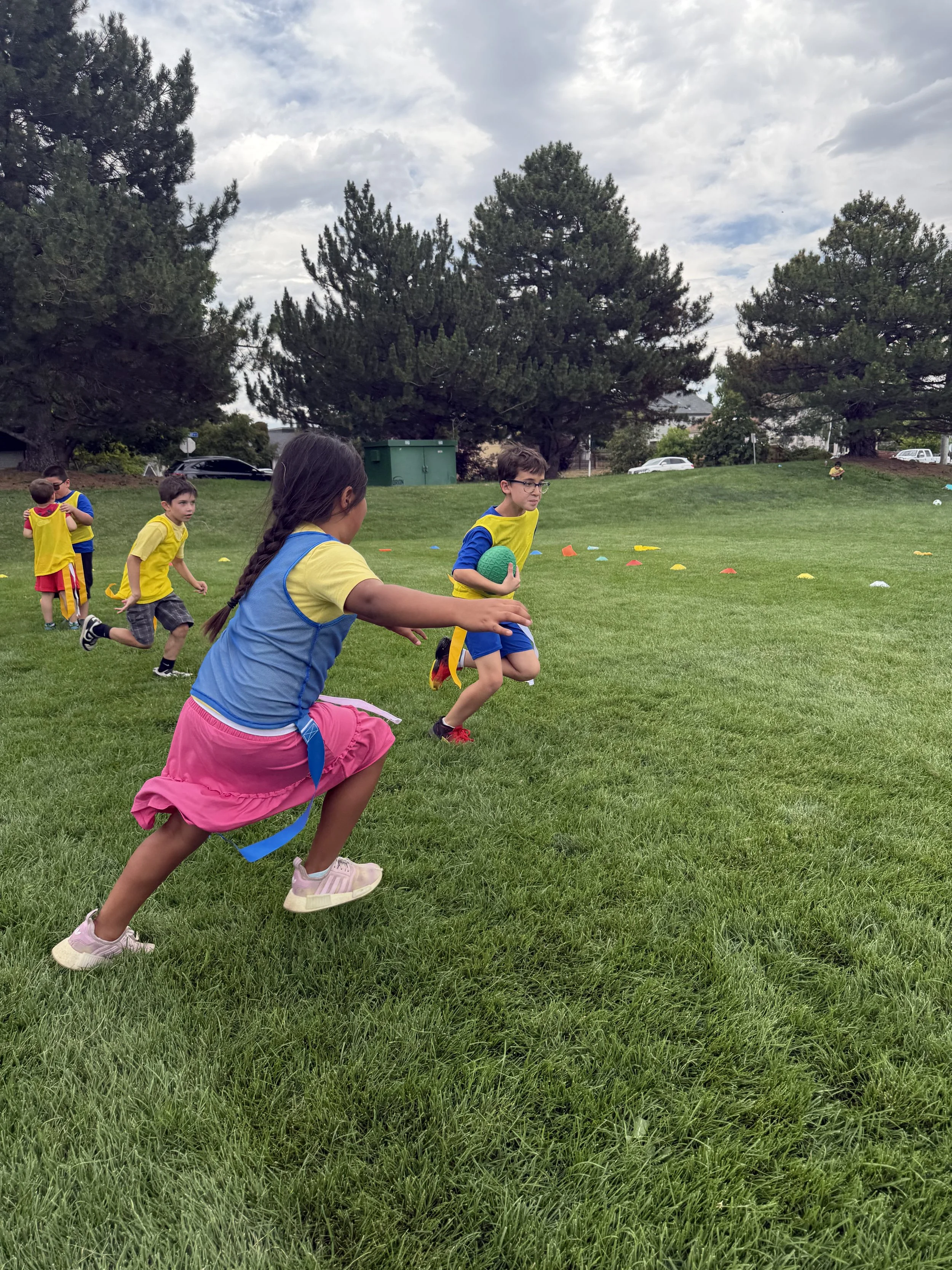 Children playing outdoor relay race on grass field, running with a green ball, participating in a sports activity.