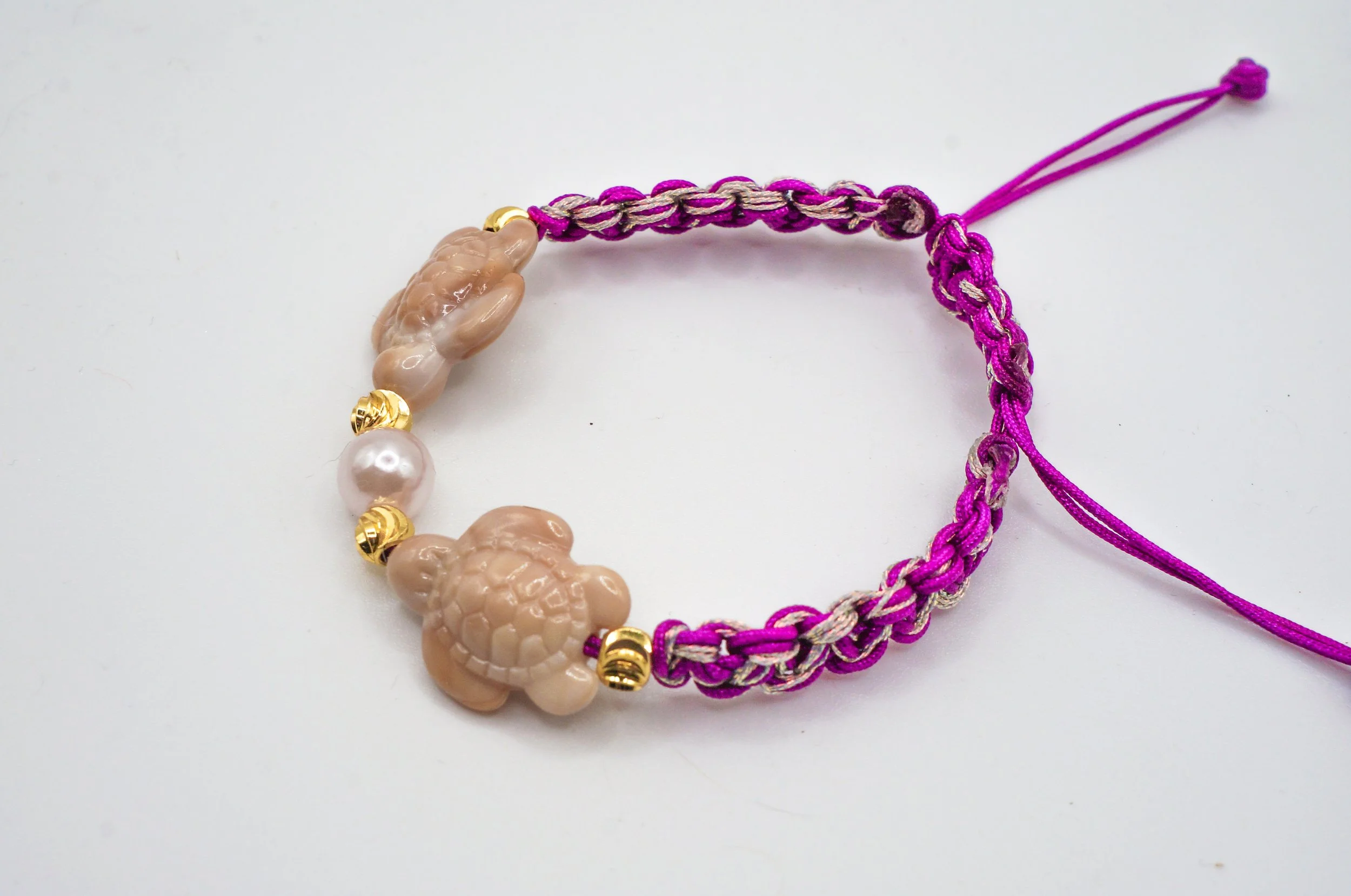 a purple woven bracelet with two seaturtles facing a pearl in the middle.