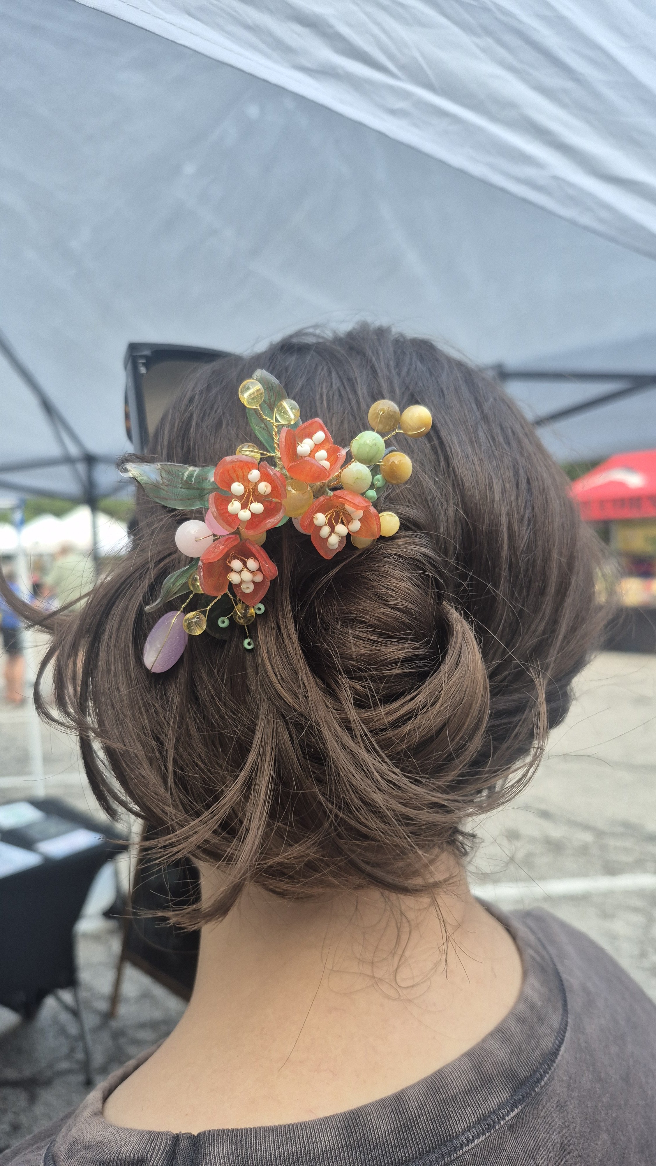  gold wavy U hair stick with red orange flowers and mixed beads holding up a bun for a customer with medium, shoulder length hair 