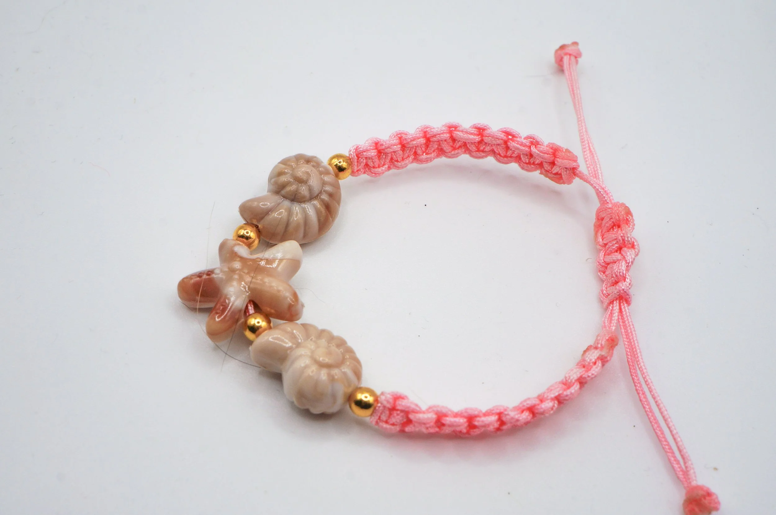 a hand woven pink macarame bracelet with a sea star and two seashells