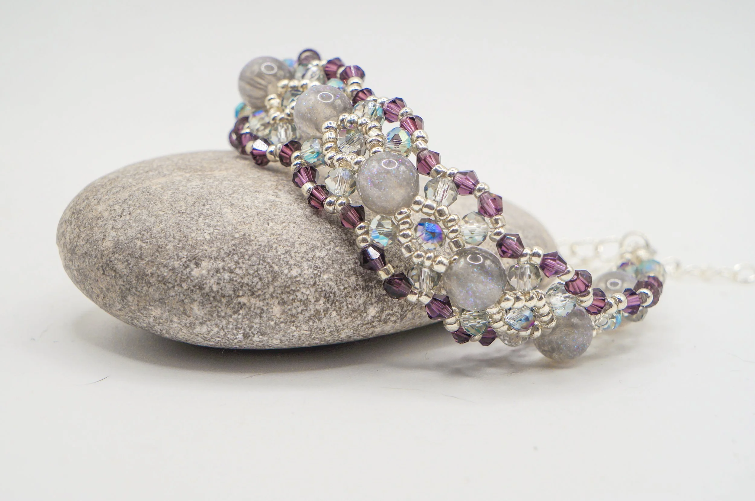 Glitter acrylic beads, iridescent faceted crystals, and small purple bicone crystals, paired with silver seed beads, weave together into this intricate bracelet.