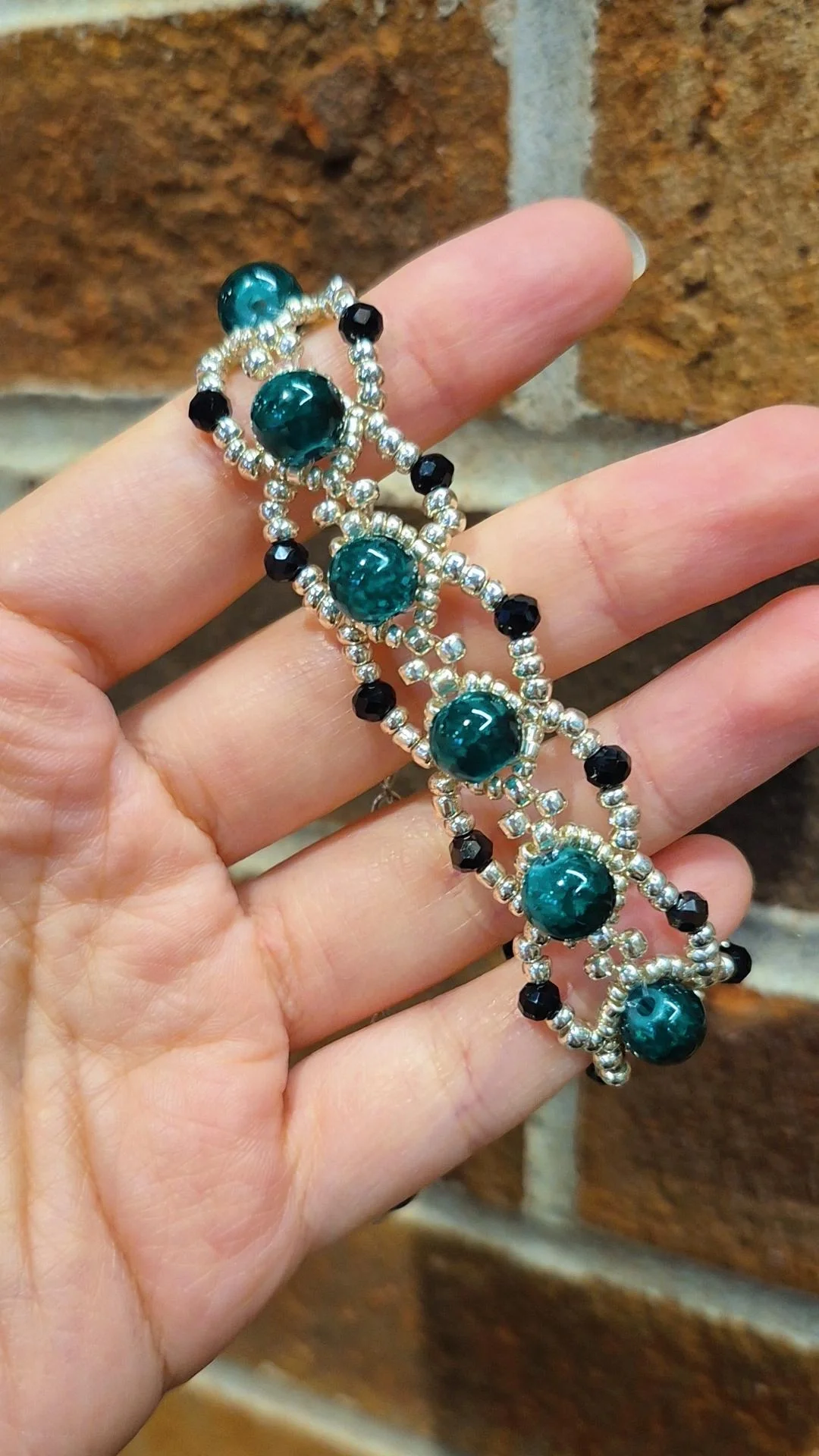a hand crafted bracelet with silver sead beads, dark faceted crystals, and dark green crackle glass beads