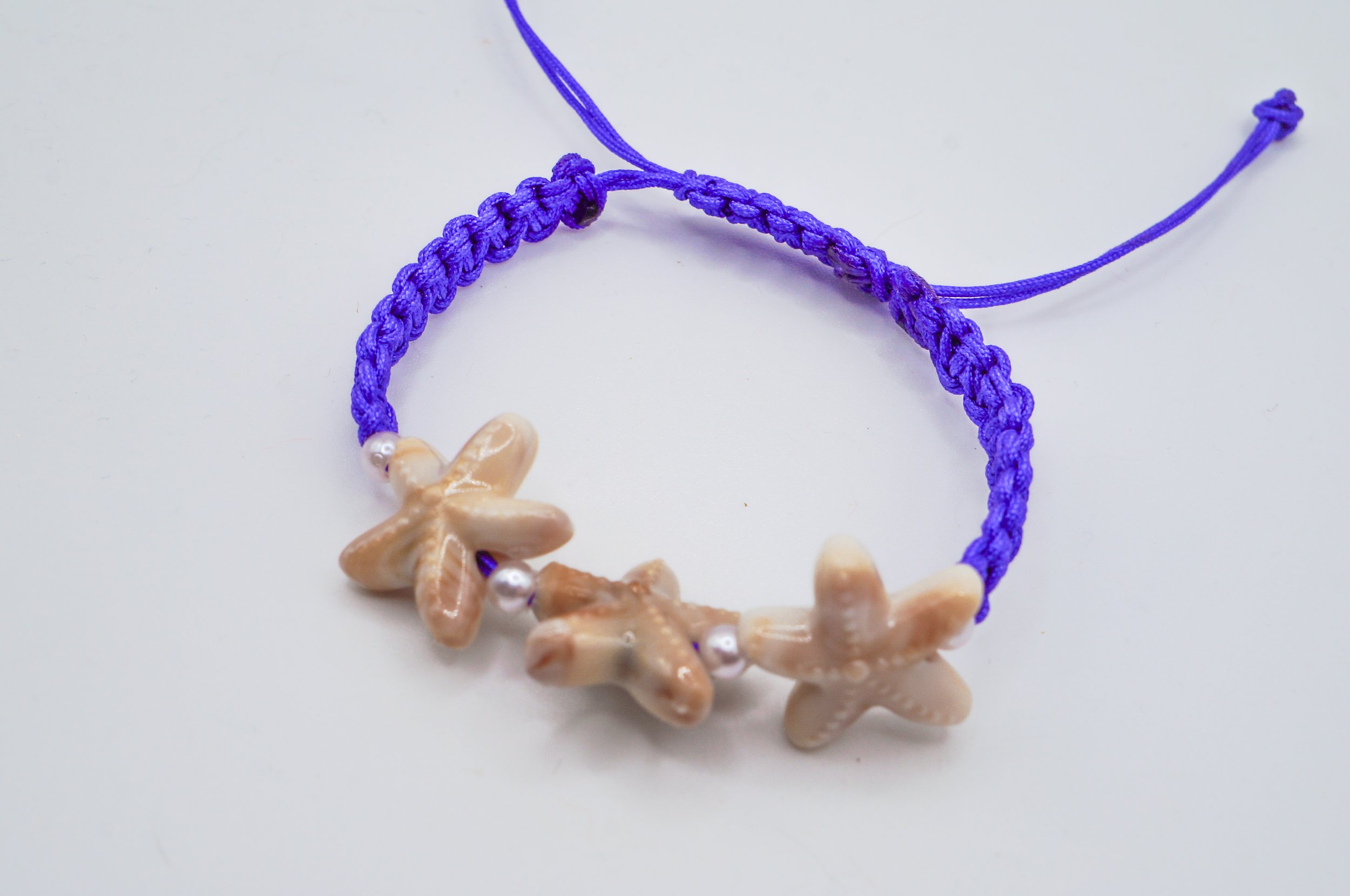 a blue macrame bracelet with three seastars connected by pearl spacers