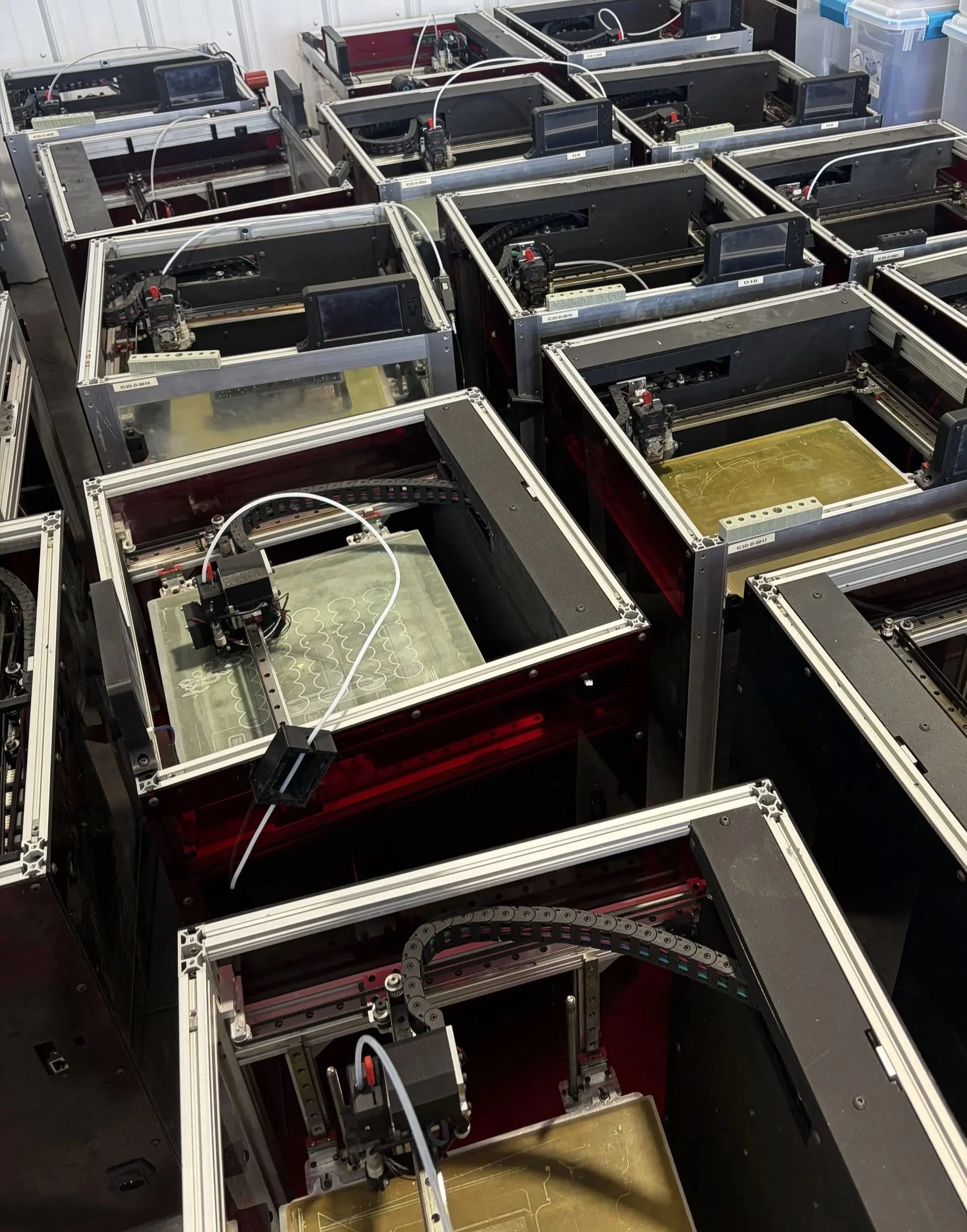 Multiple 3D printers with metal frames and components, some with heated beds, in a laboratory or workshop setting.
