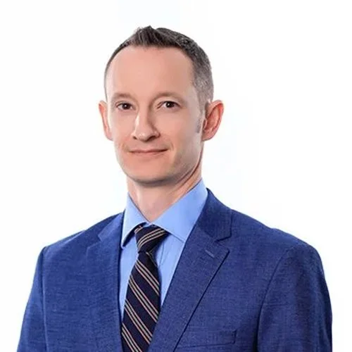 A man in a blue suit and striped tie smiling against a white background.