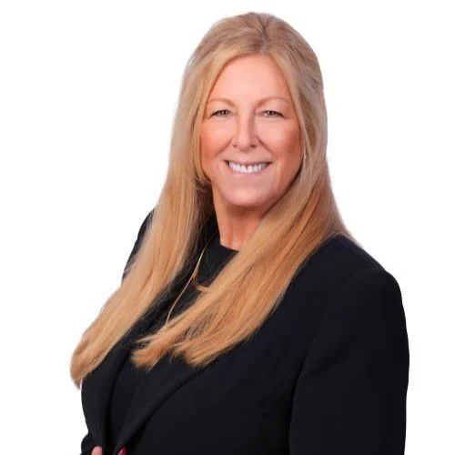 A man with a bald head and blue eyes wearing a checkered blazer and a white shirt, posing against a white background.