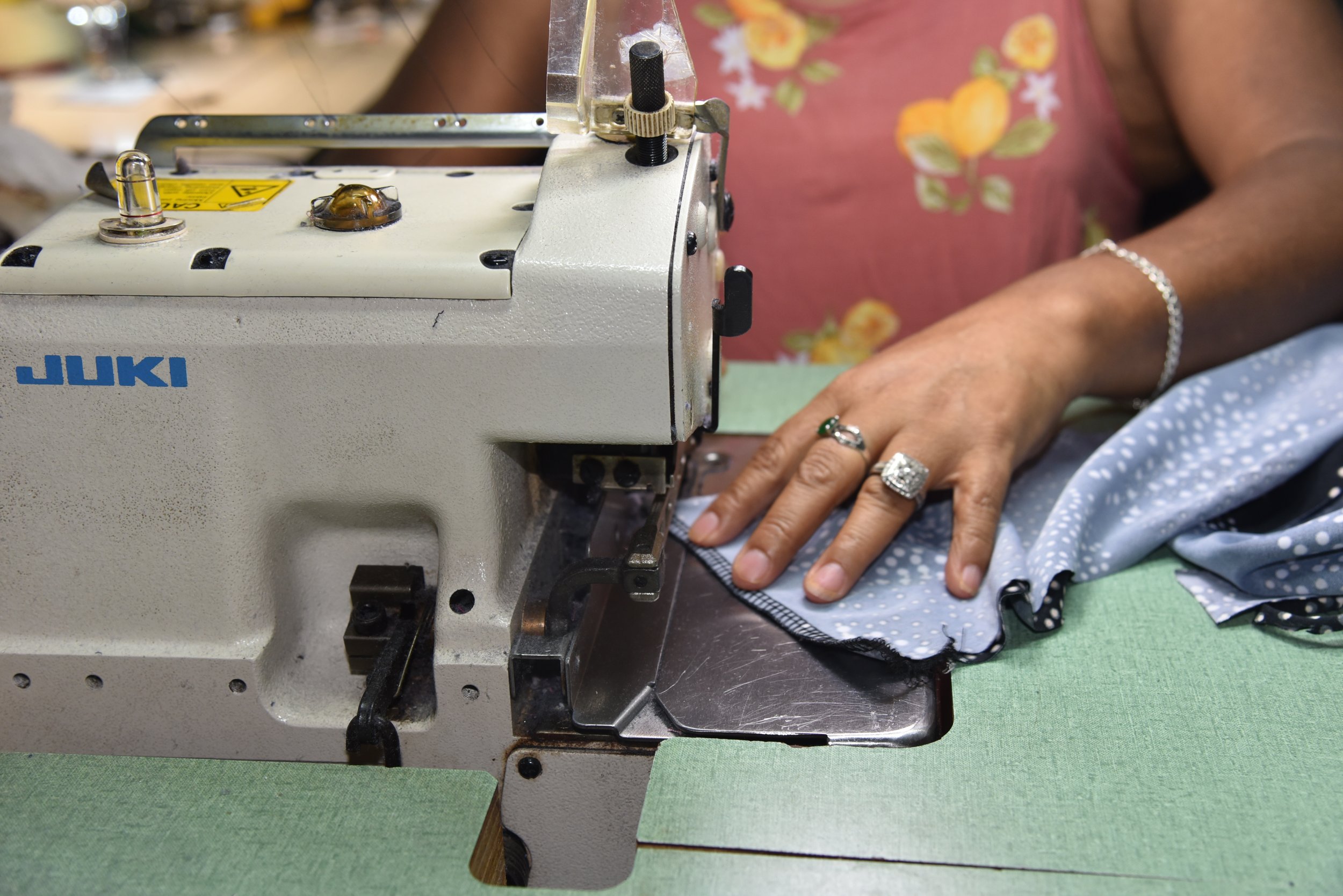Close-up of a person sewing fabric with a Juki sewing machine, wearing rings and a bracelet.