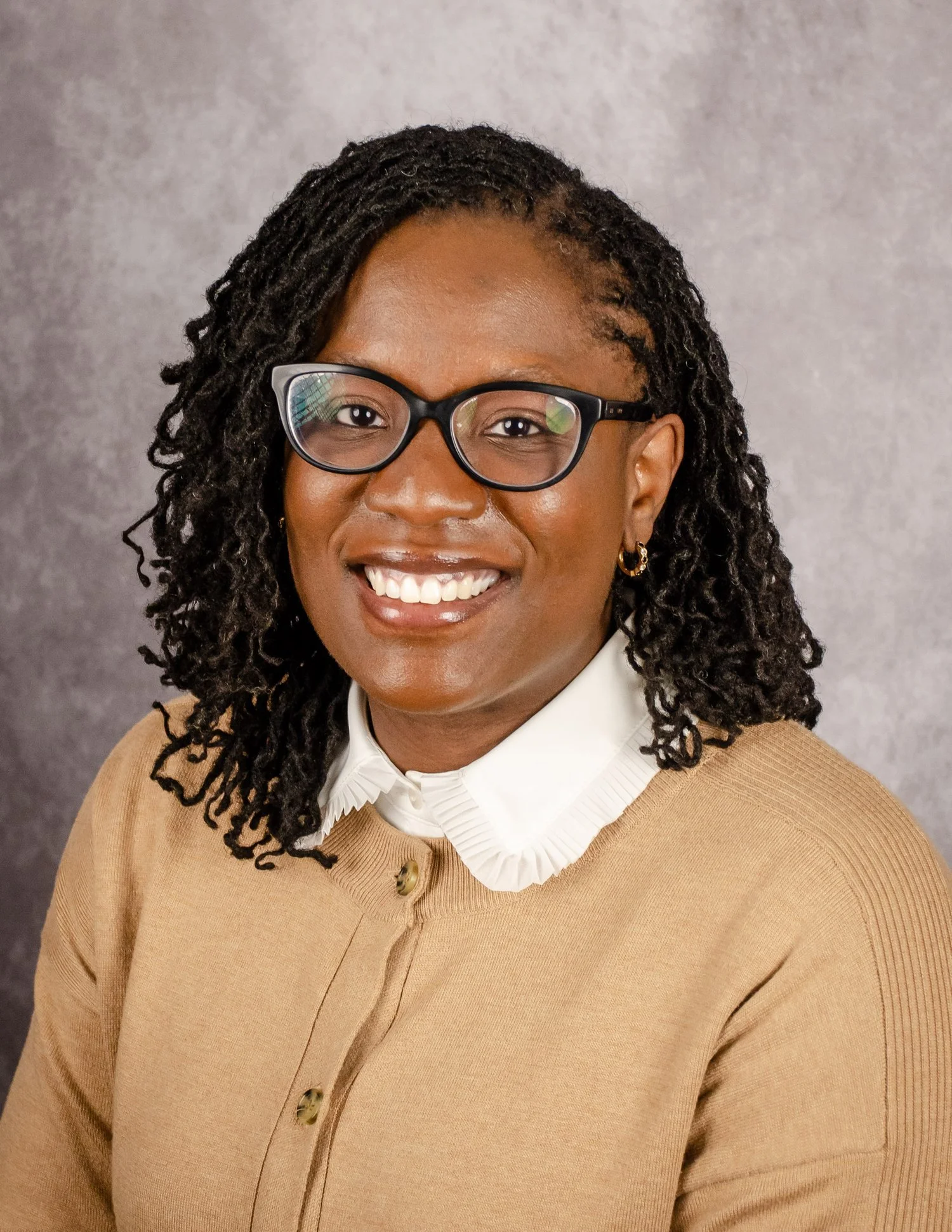 Portrait of a smiling woman with long brown hair wearing a beige blazer and a white blouse.