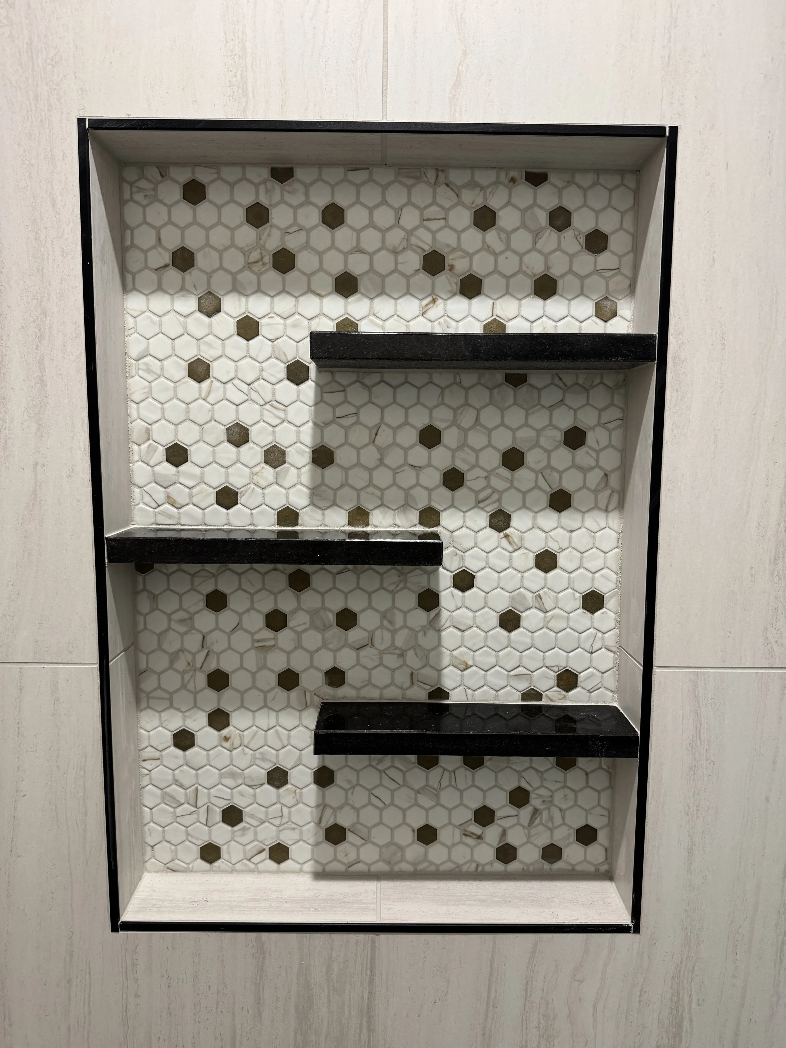 Tiled shower niche with black shelves and a white-and-gold hexagon-tile background.