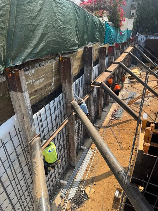 Construction workers are installing rebar and formwork for a concrete wall at a construction site.