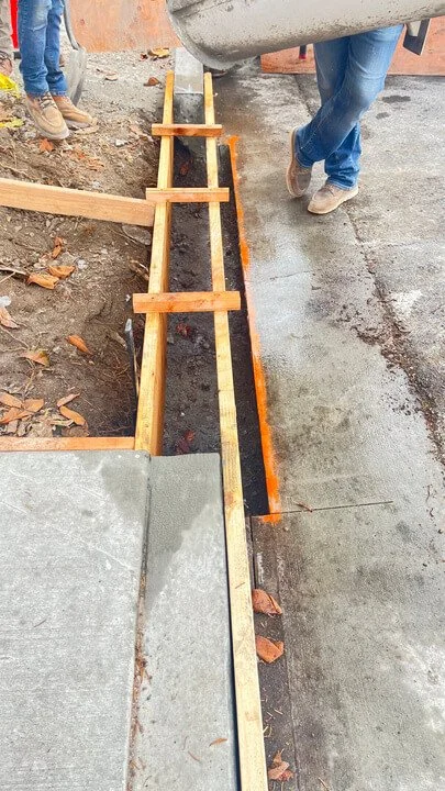 Construction site with wooden forms and concrete slab, workers' legs visible, preparing for concrete pouring.