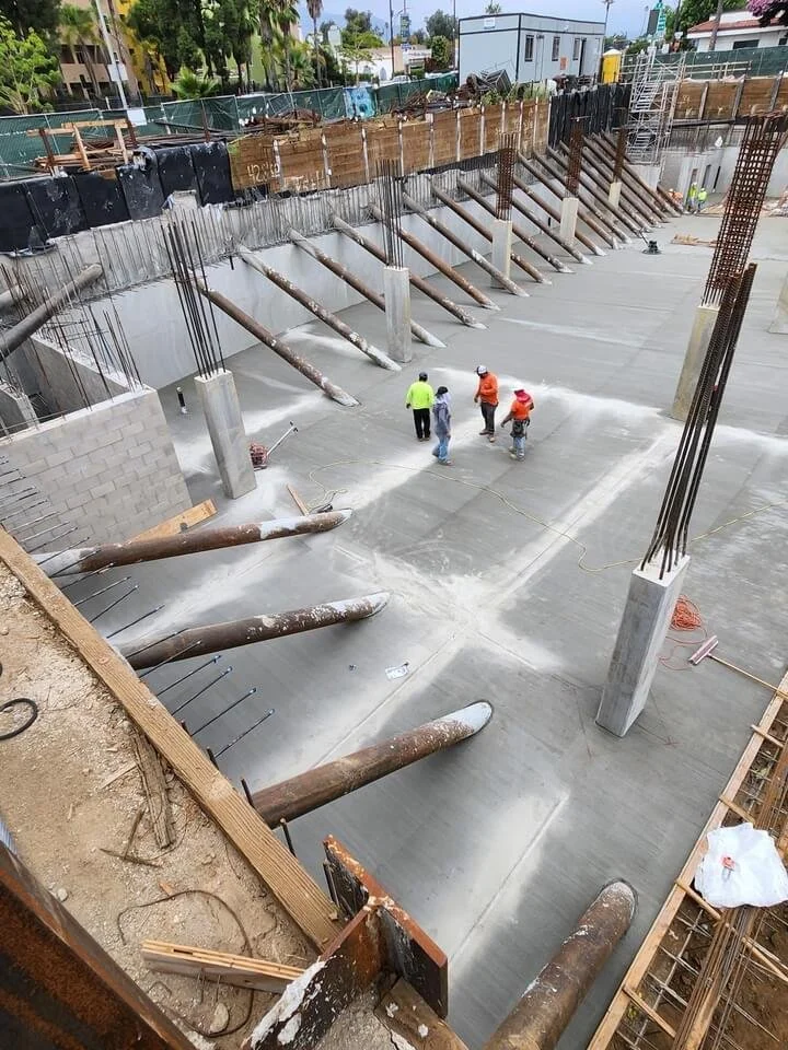 Construction workers working on a concrete foundation of a building, with support beams and rebar in place.