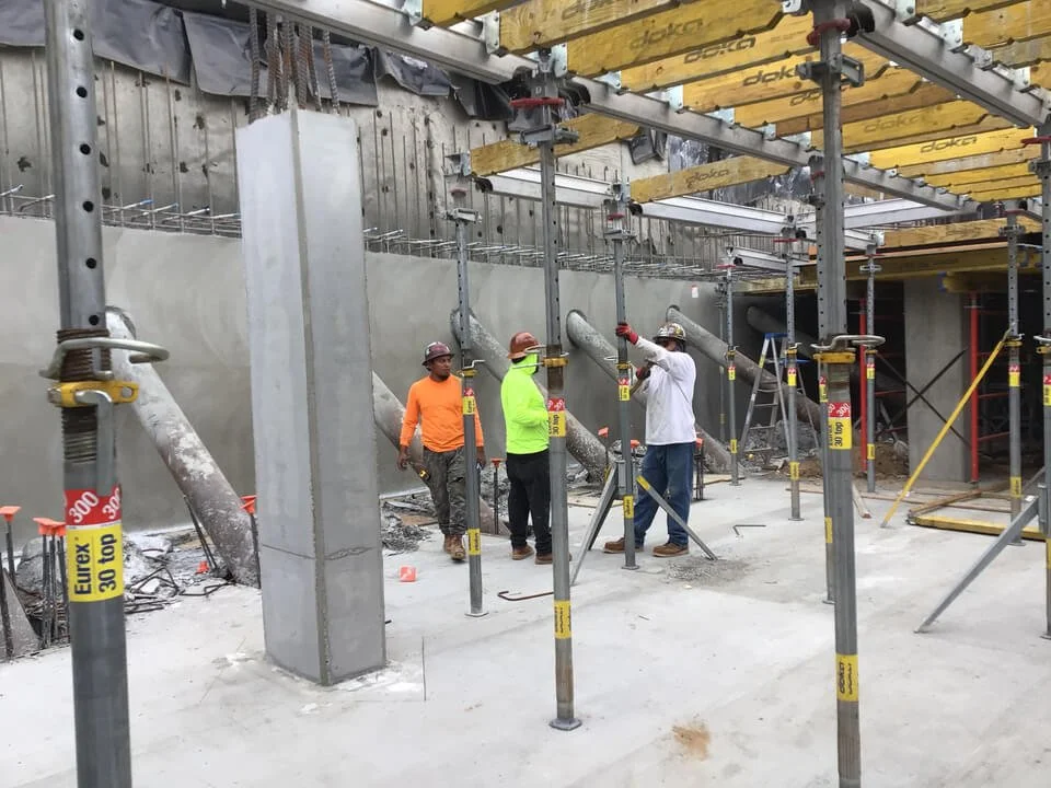 Construction workers on a building site, working with and inspecting metal ductwork for heating or ventilation system installation.