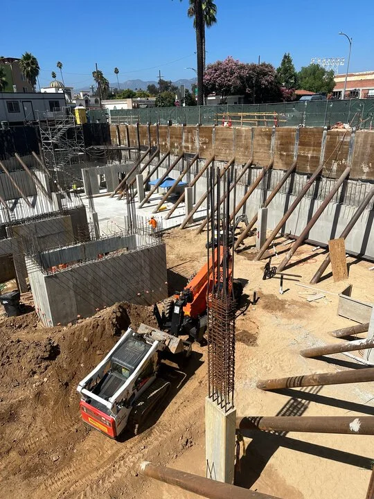 Construction site with heavy machinery, steel reinforcement, and wooden supports for building foundation.
