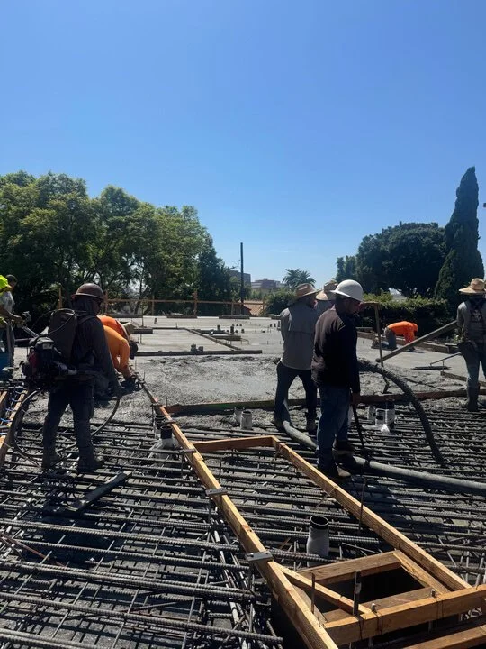 Construction workers pouring concrete on a building site with rebar framework under a clear blue sky.