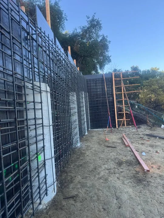 Construction site with rebar framework and wooden support structures for a concrete wall, outdoor setting with trees in the background