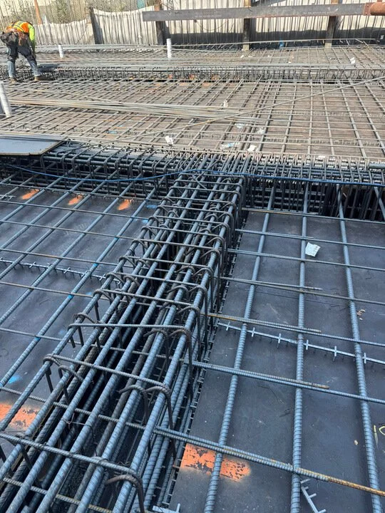 Construction site with steel rebar framework for concrete pouring, worker in safety gear in the background.