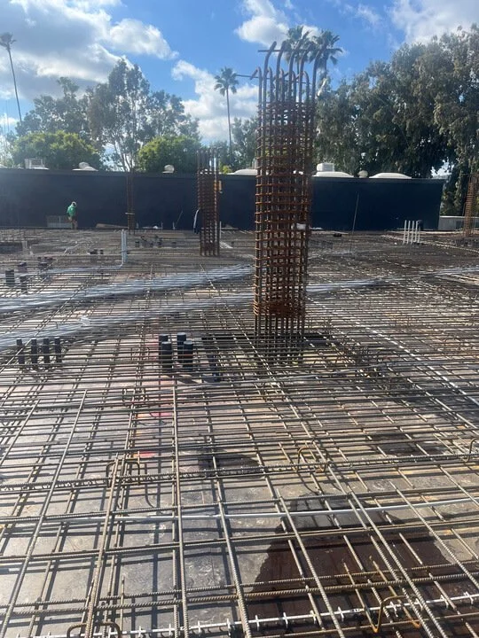 Construction site with steel rebar grid and vertical rebar columns for a building foundation.
