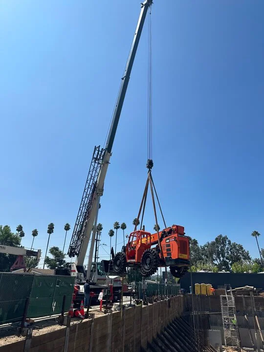 A crane lifting a small orange off-road vehicle into a construction site