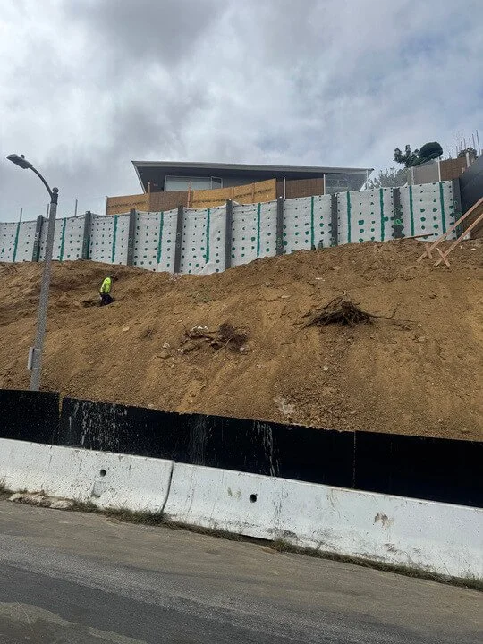 Construction worker on a dirt hillside near a new building with a temporary retaining wall.