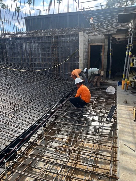 Construction workers installing rebar on a building site under a partly cloudy sky.