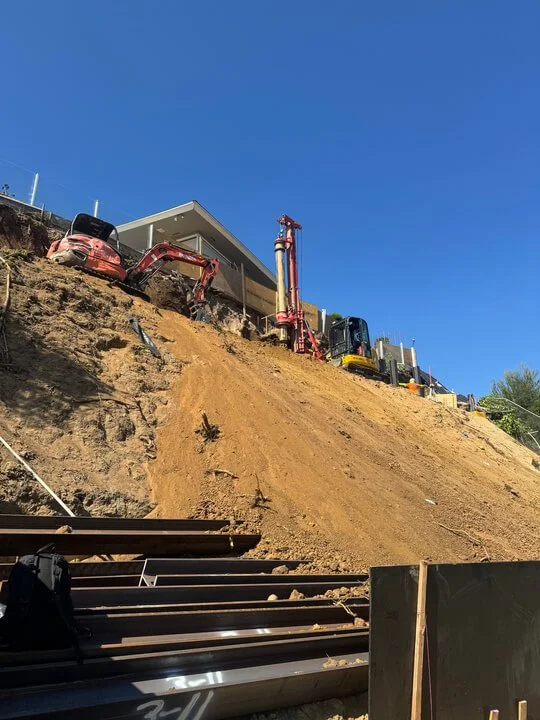 Construction equipment on a hillside, with excavators and a building under construction, after a landslide.