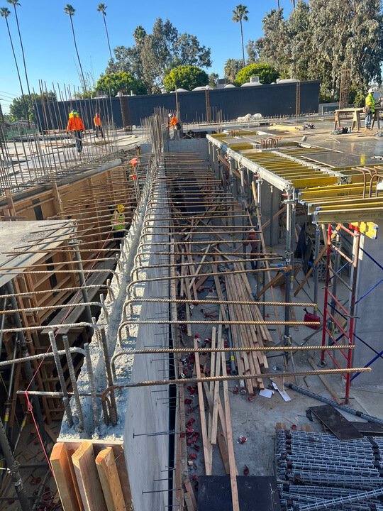 Construction site with workers and steel rebar, wood, and scaffolding during building process.