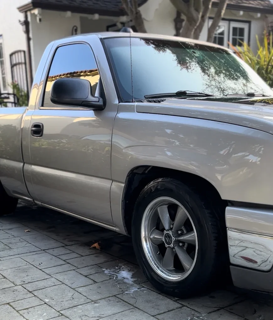 Silver pickup truck parked on a paved driveway in front of a household.