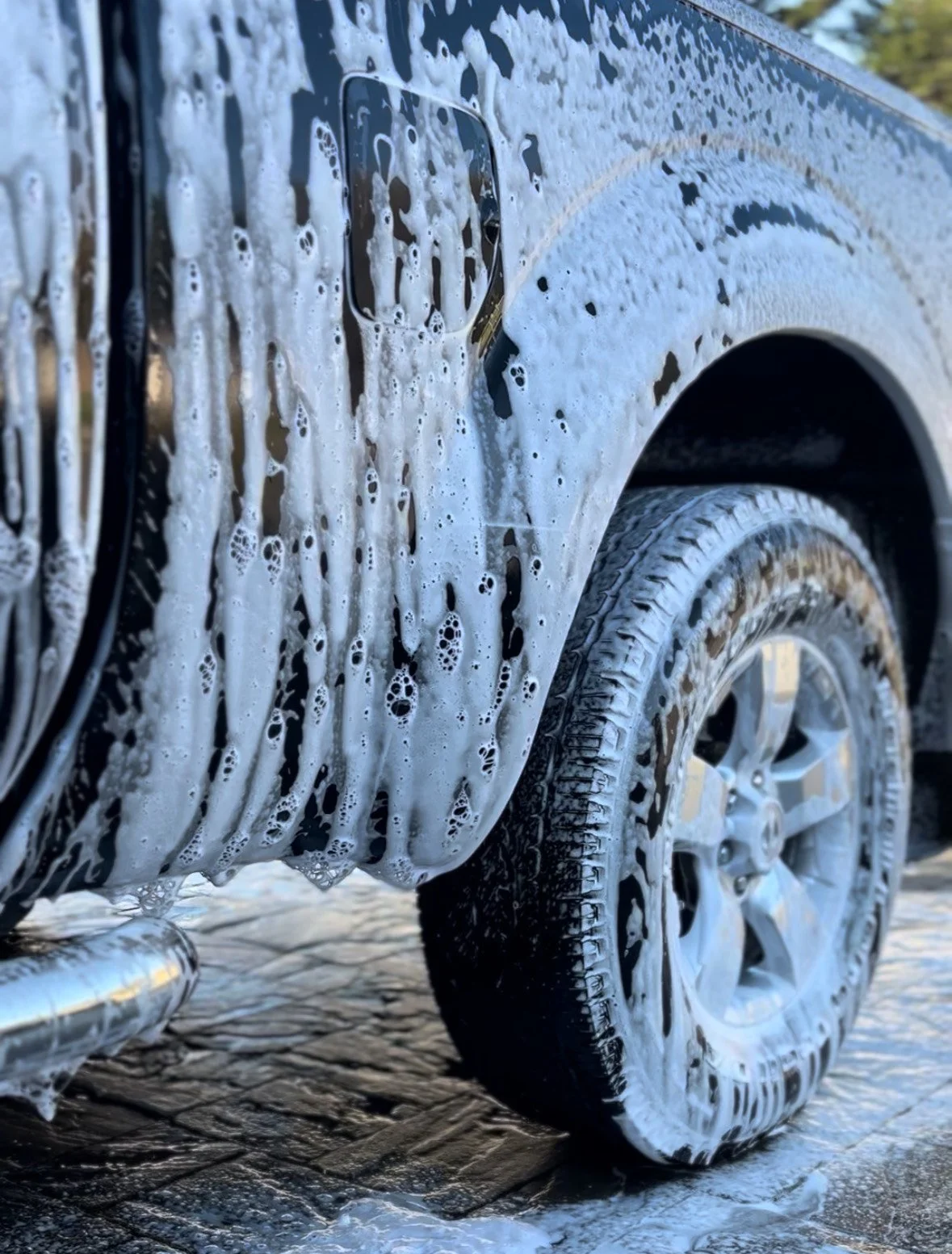 Close-up of a white BMW car parked on a brick driveway, showing the front right side including the wheel and headlight.