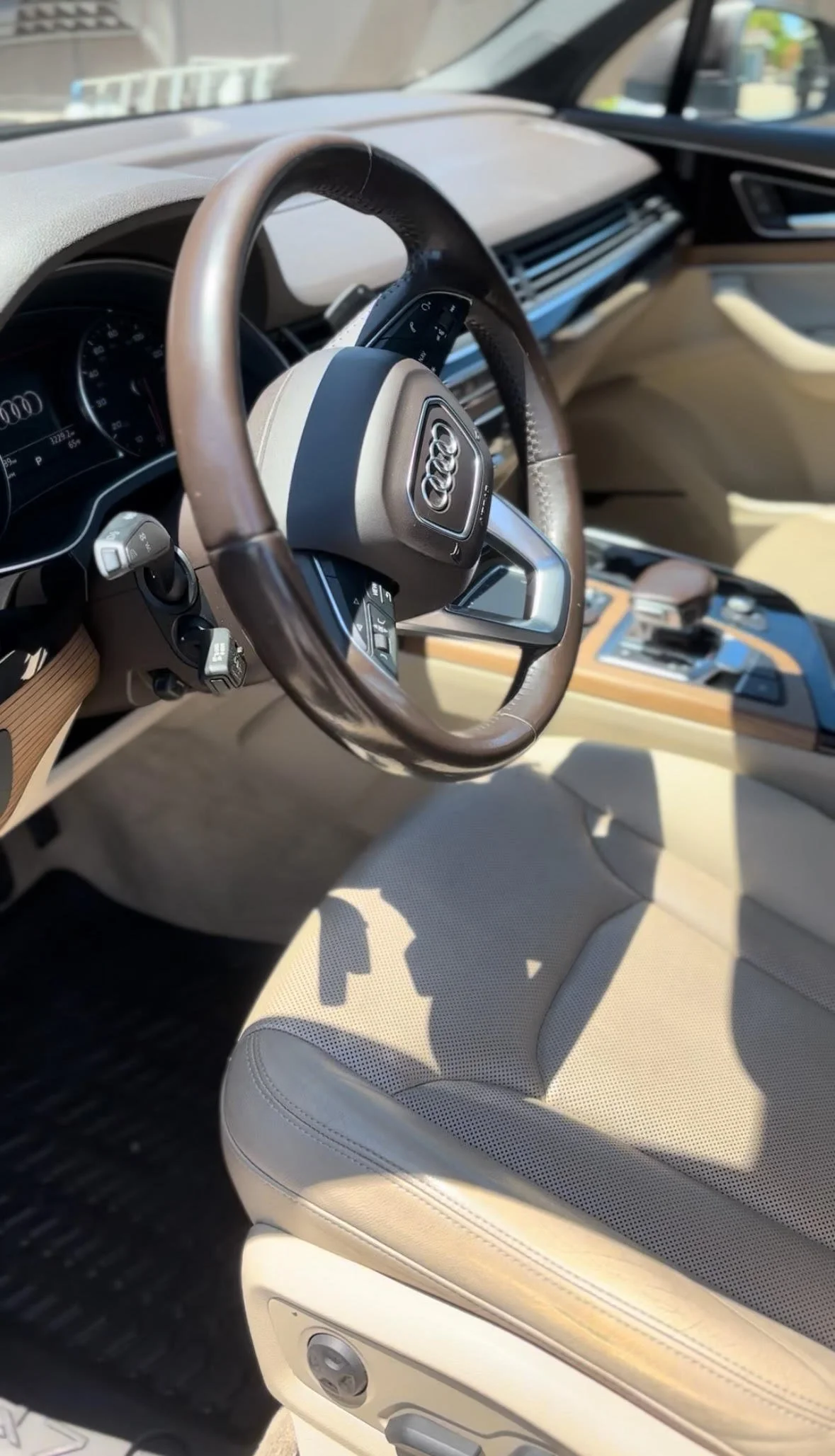 Interior of an Audi vehicle showing the steering wheel, dashboard, center console, and front seat with light-colored upholstery.