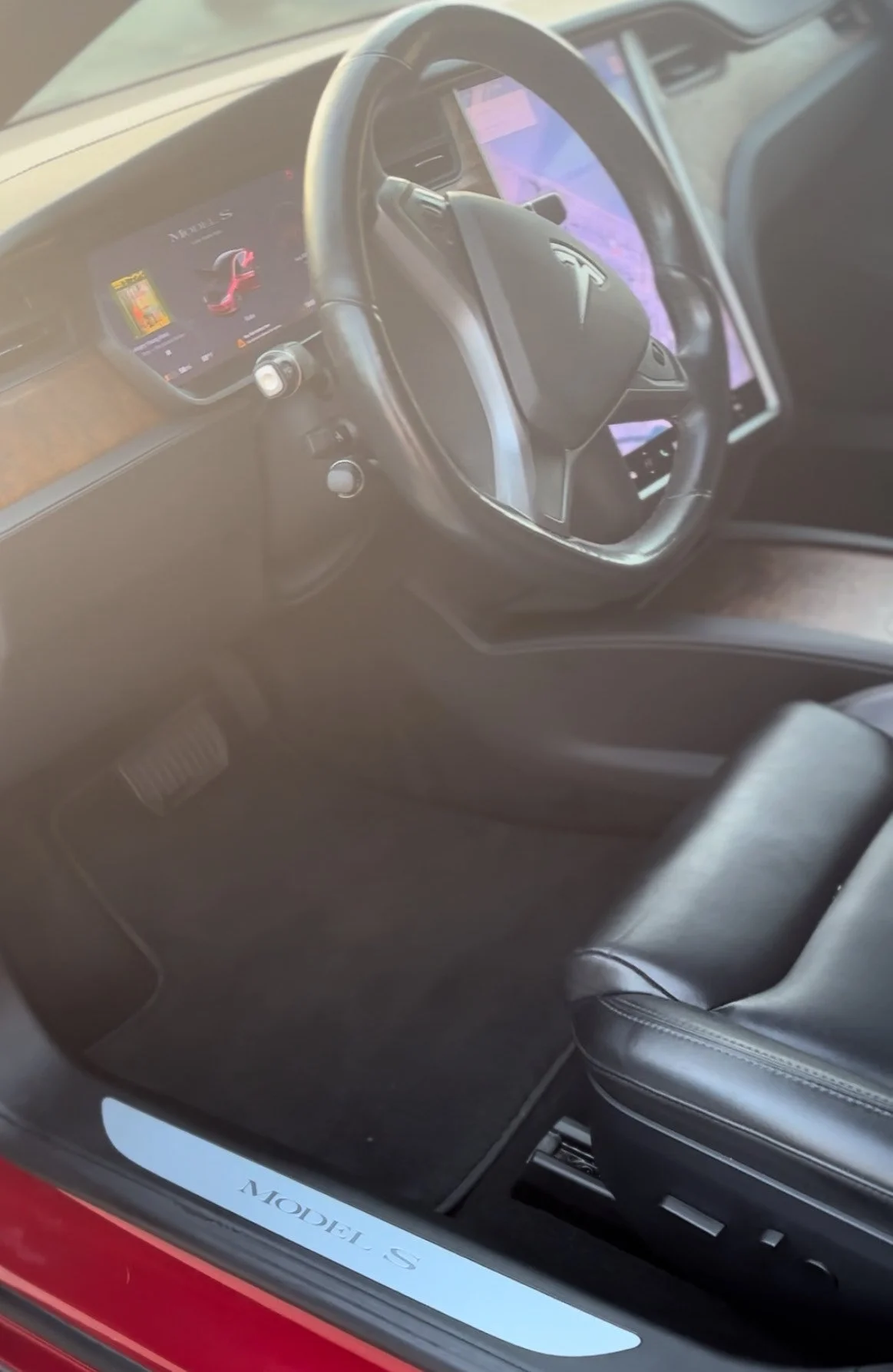 Interior of a Tesla Model S with a steering wheel, dashboard, and central touchscreen display visible.