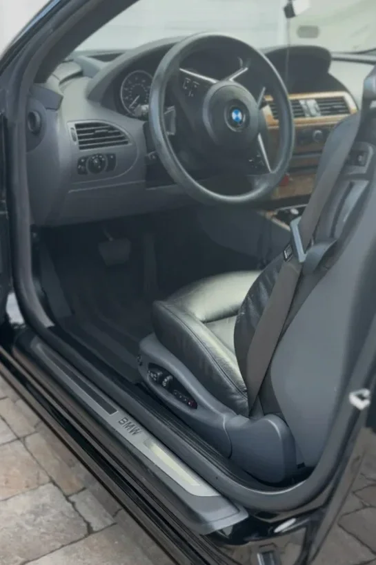 Interior of a BMW car showing the driver's seat, steering wheel with BMW logo, dashboard, and part of the center console.