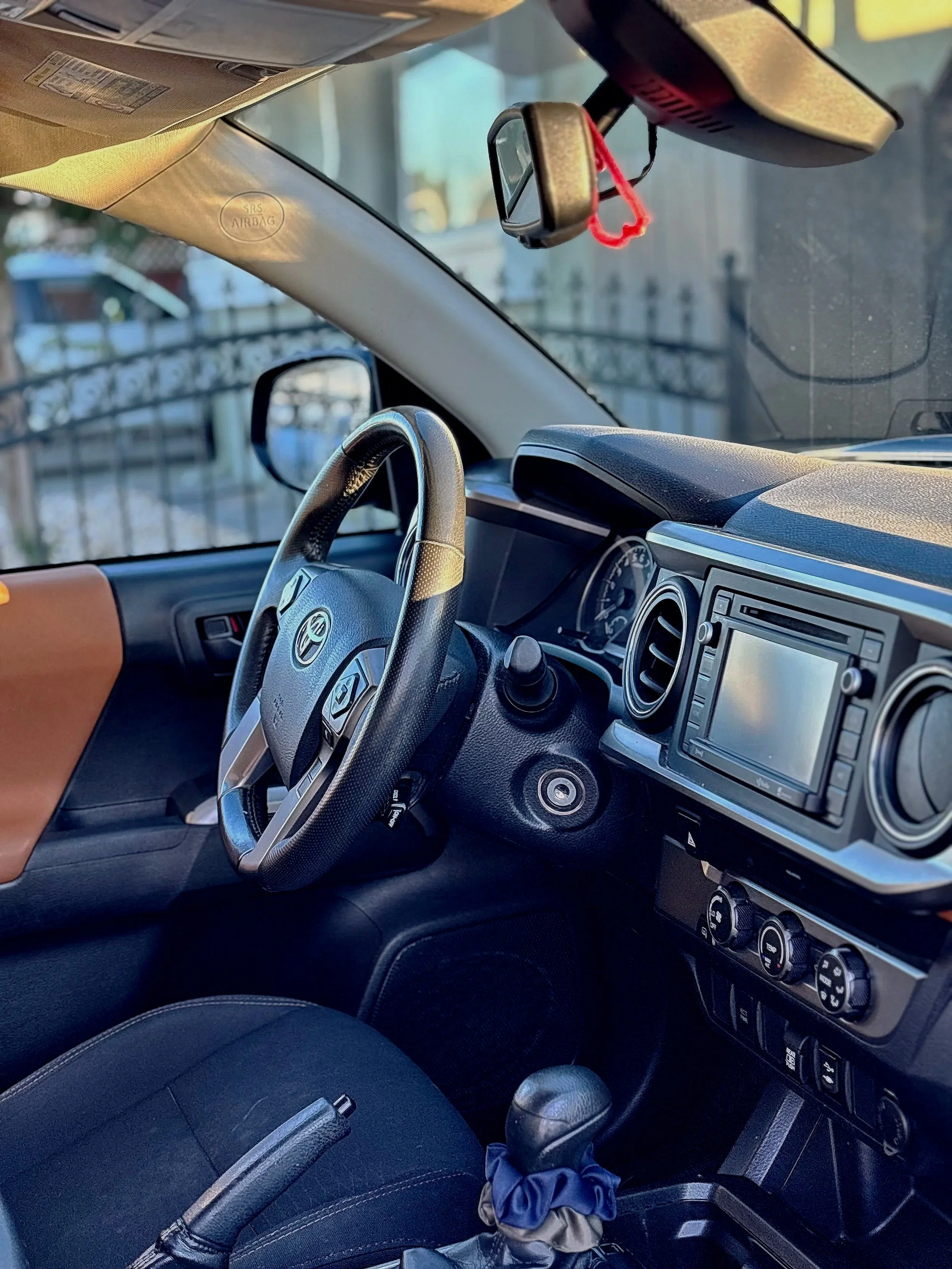 Interior of a vehicle showing the steering wheel, dashboard, and front seats, with a rearview mirror and sun visor.