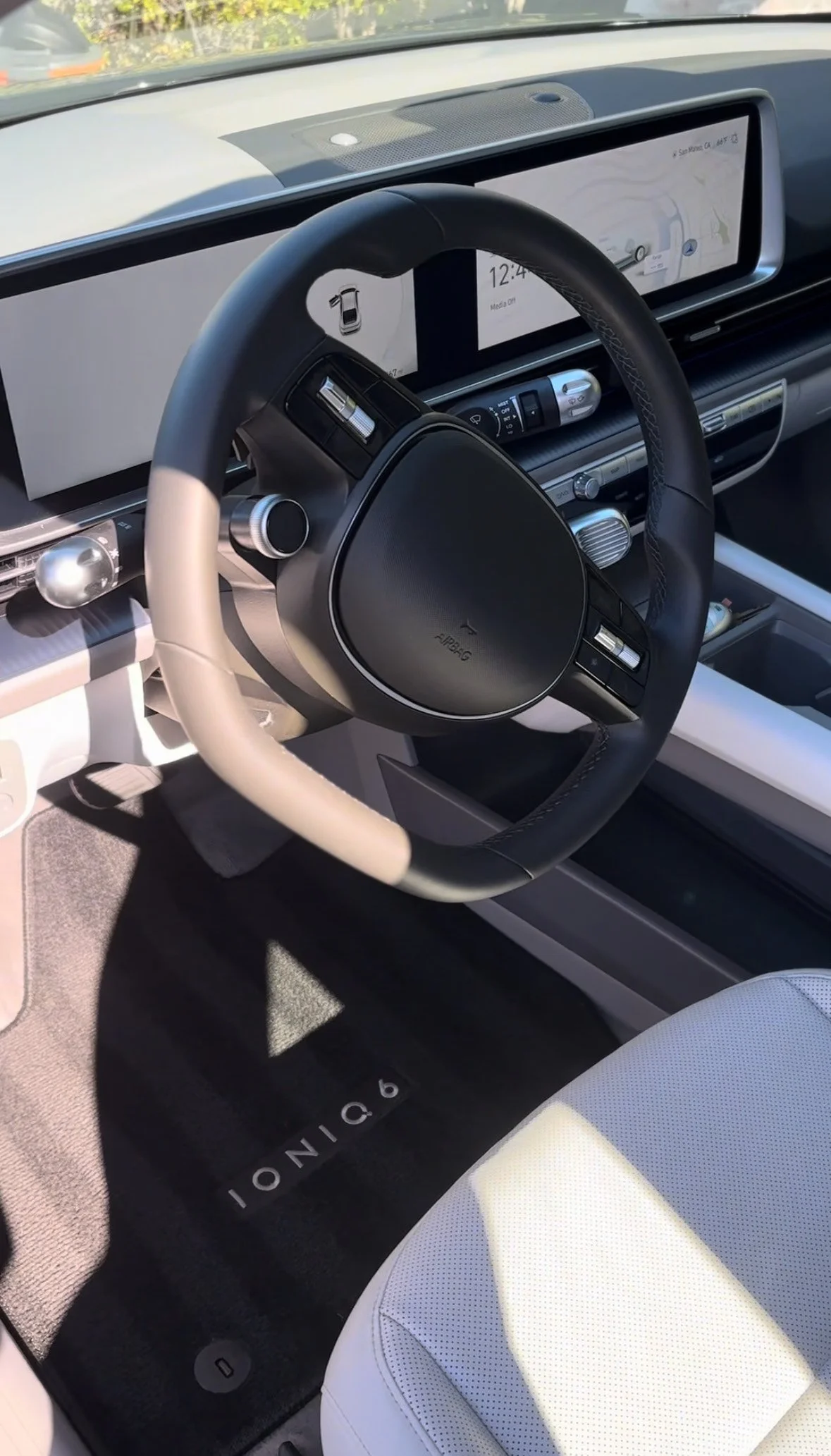 Interior view of a modern car with a black and beige steering wheel, a digital display screen, and a black floor mat with the word 'delion' on it. The dashboard includes various controls and a map display.