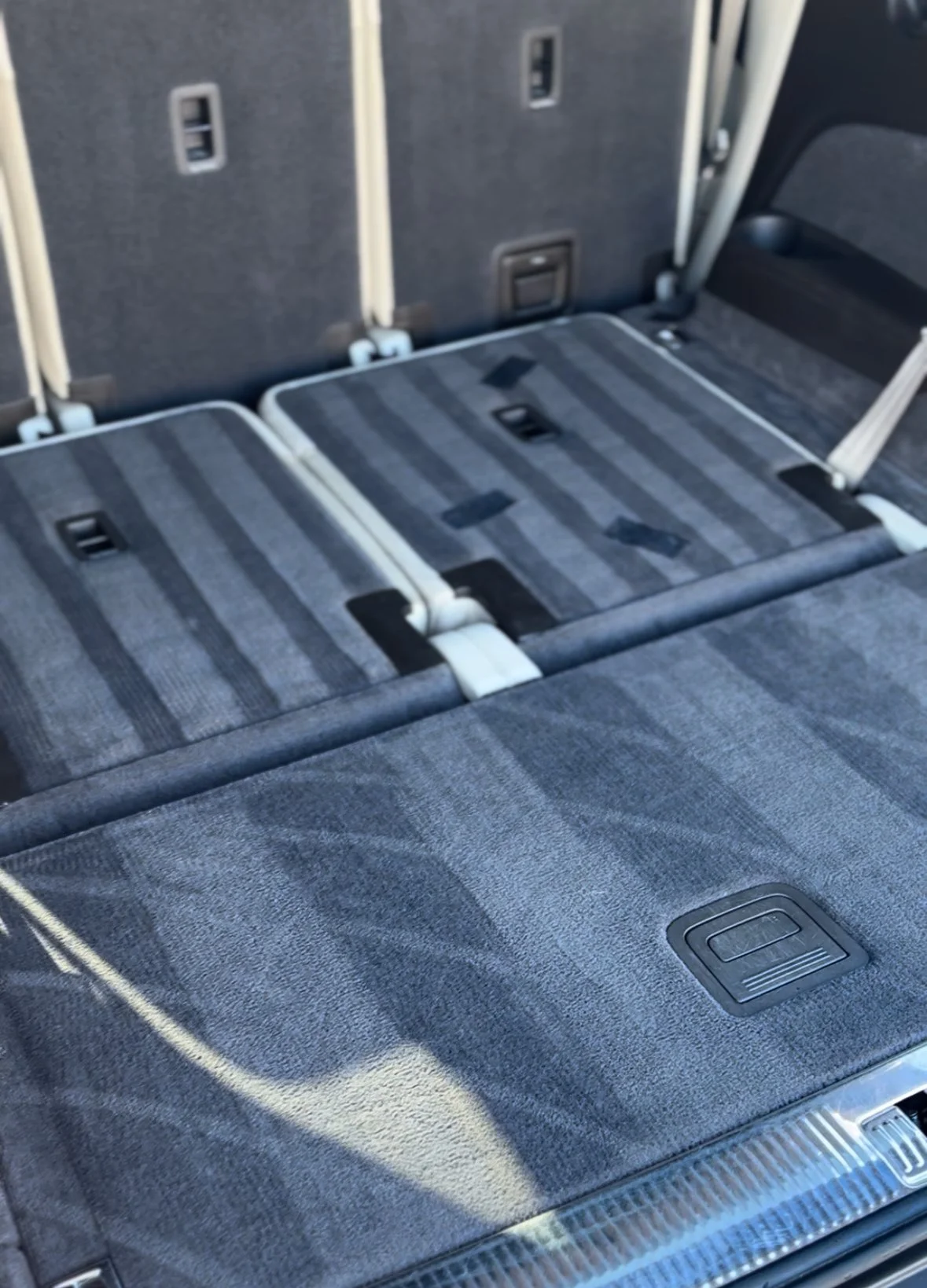 The interior of a vehicle showing the folded third-row seats in a dark gray and black fabric upholstery.