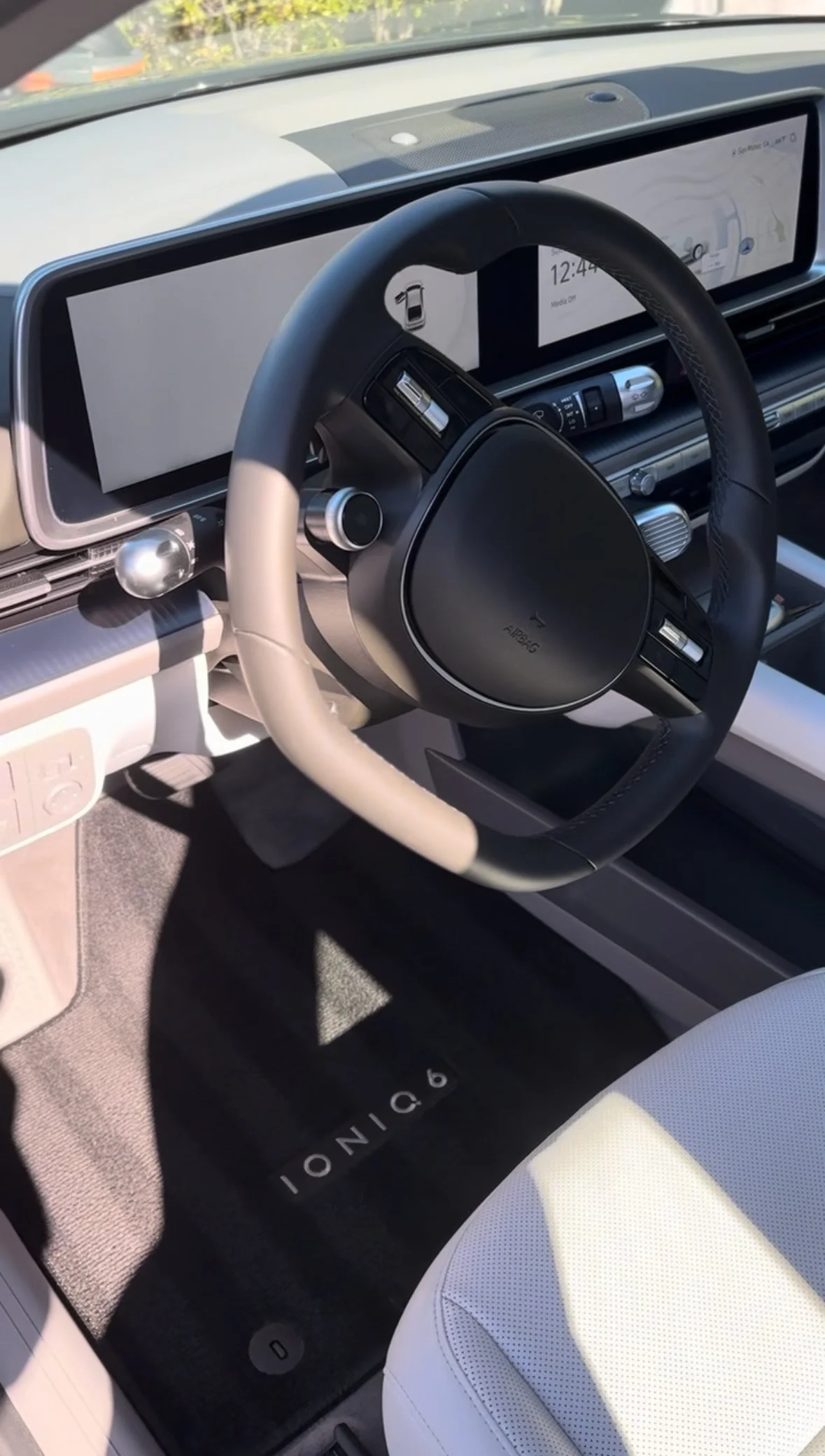 The interior of a futuristic car dashboard with a digital steering wheel, large infotainment screens, and modern controls, with an IonIQ branded floor mat.