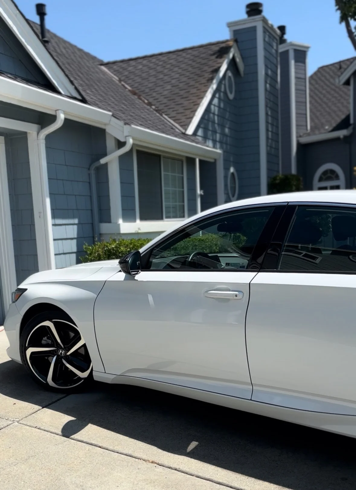 A white sedan parked in front of a blue house with a gray shingled roof on a sunny day.
