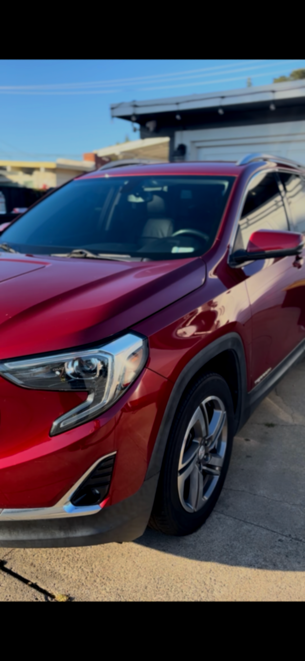 A red SUV parked on a driveway in front of a house with a clear blue sky in the background.