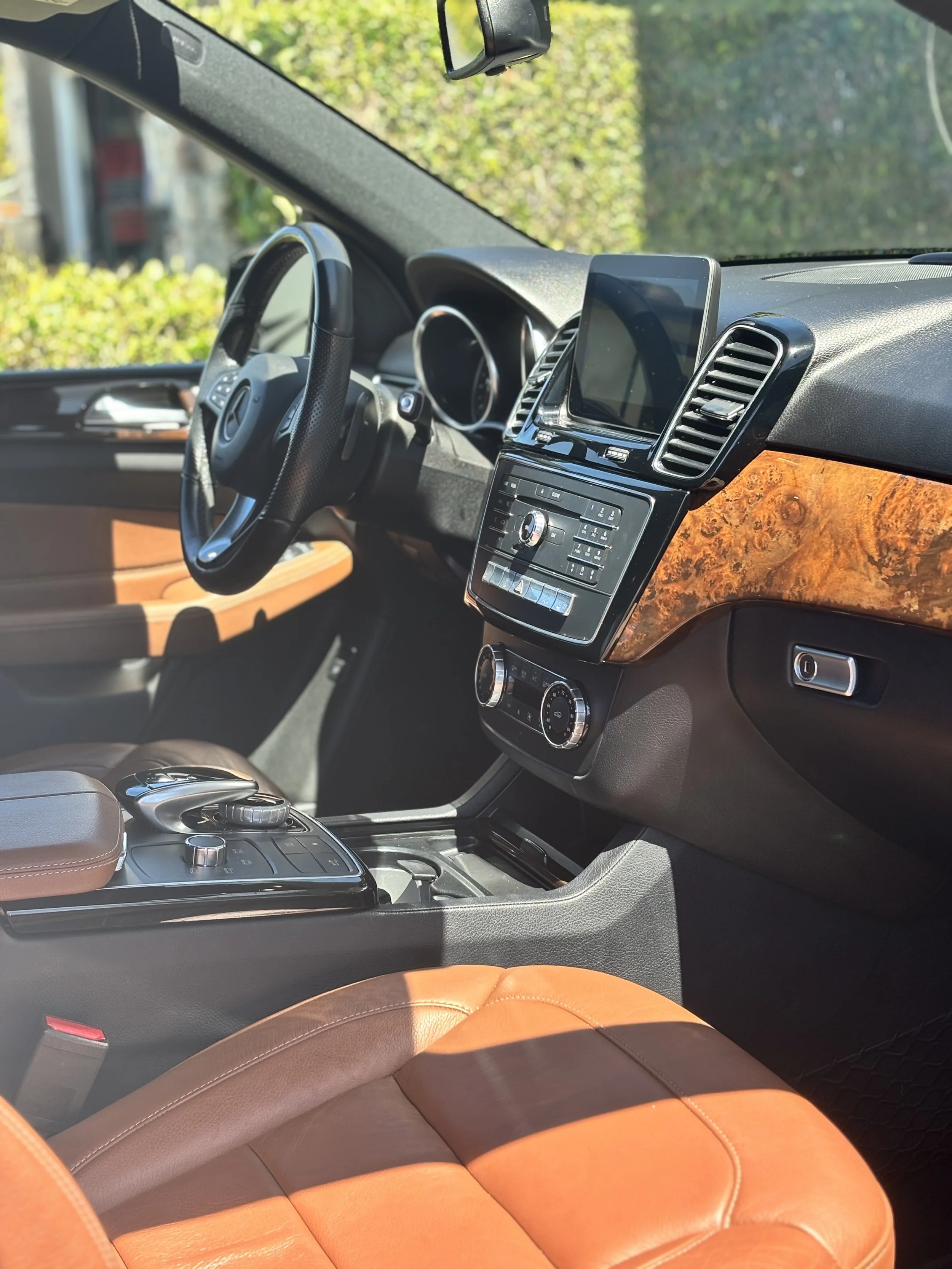Interior of a luxury vehicle with a steering wheel, infotainment screen, wood trim, control panels, and leather seats.