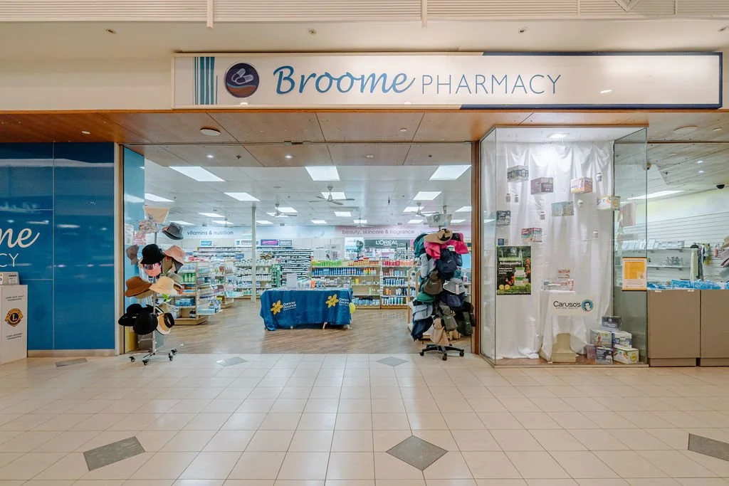 Entrance of Broome Pharmacy inside a shopping mall, with shelves of products and hats displayed near the entrance.
