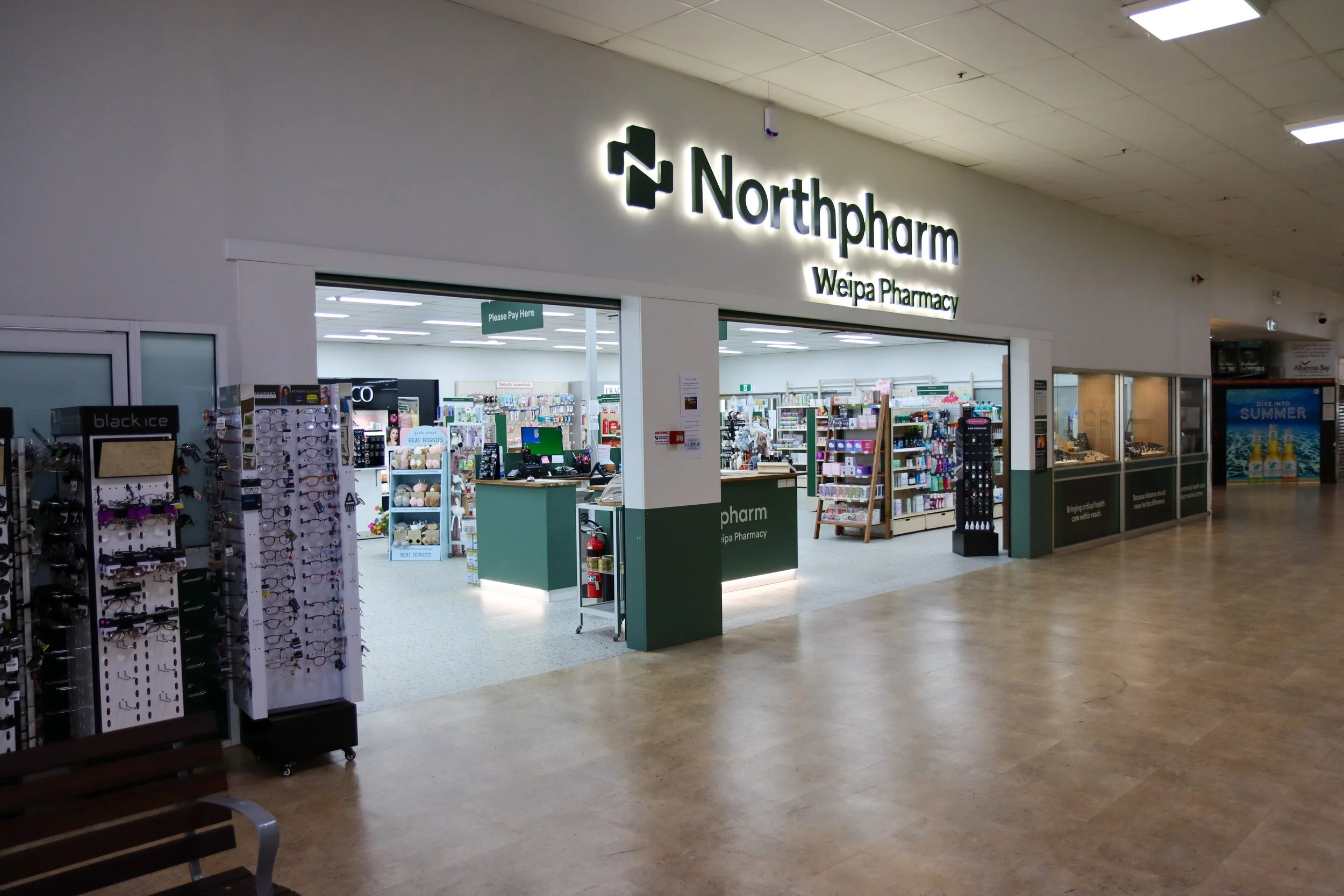 Entrance to Northpharm Weipa Pharmacy inside a shopping mall, with a display of sunglasses on the left and shelves of products inside.