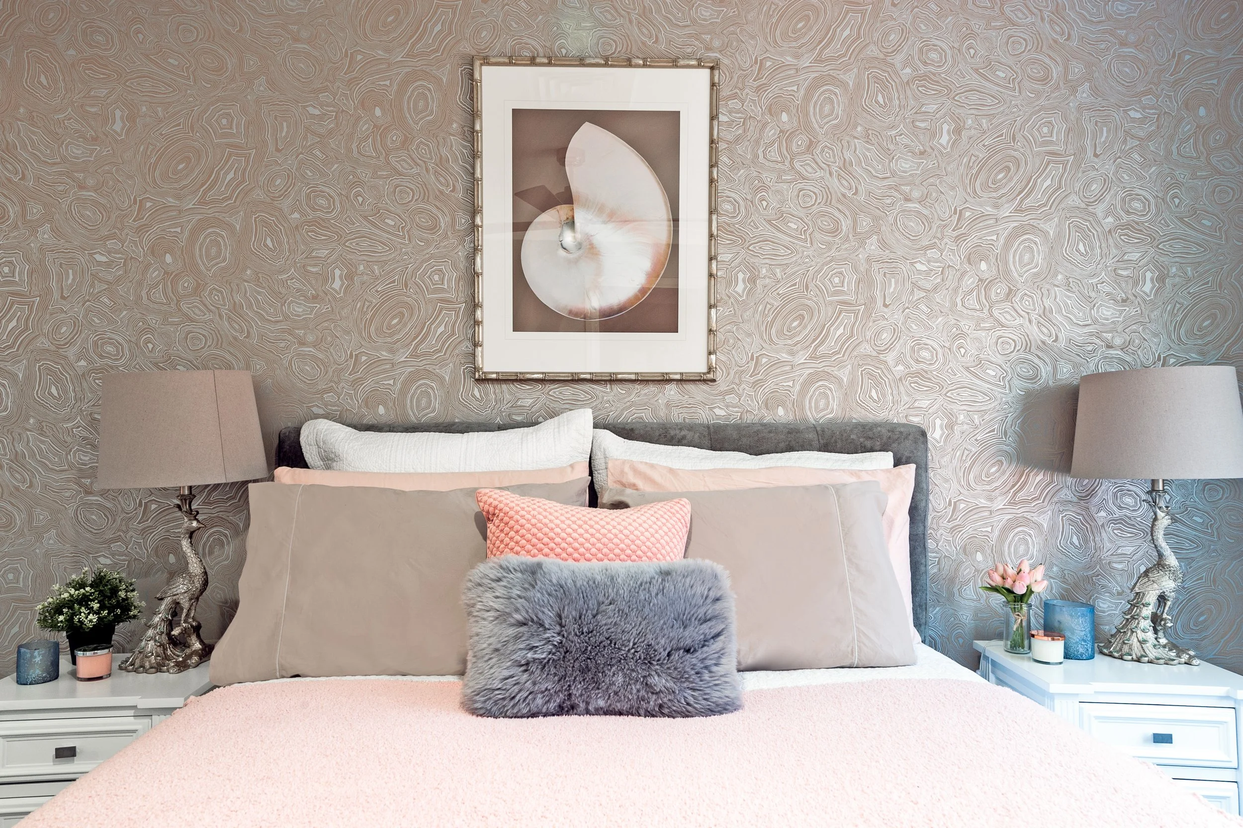 A cozy bedroom with a bed, decorative pillows, two bedside tables with lamps, and artwork on the wall.