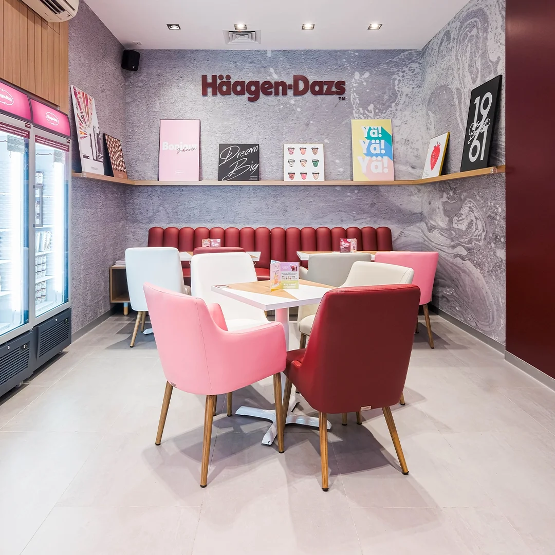 Inside a Häagen-Dazs ice cream shop with colorful chairs, a table, and wall decorations including posters and the Häagen-Dazs logo.