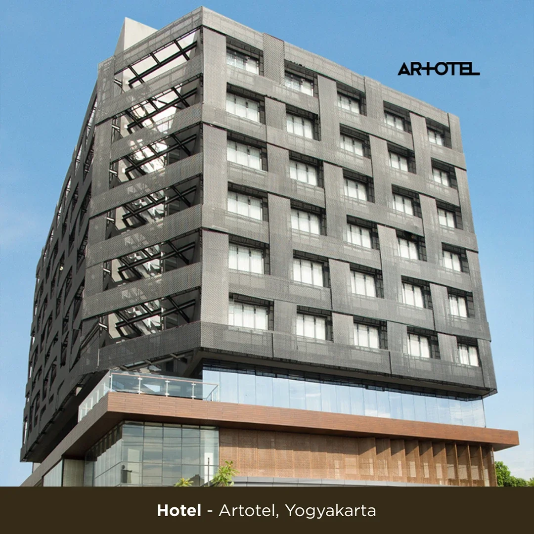 A modern multi-story hotel building called Artotel in Yogyakarta, with a gray facade, multiple windows, and an external staircase on the side, set against a clear blue sky.