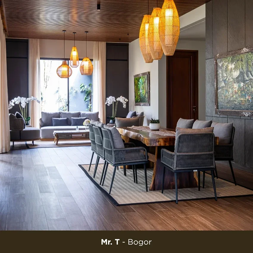 Modern living and dining room with wooden ceiling, hanging wicker pendant lights, gray sofas, a wooden dining table with six chairs, potted plants, and artwork on the walls.