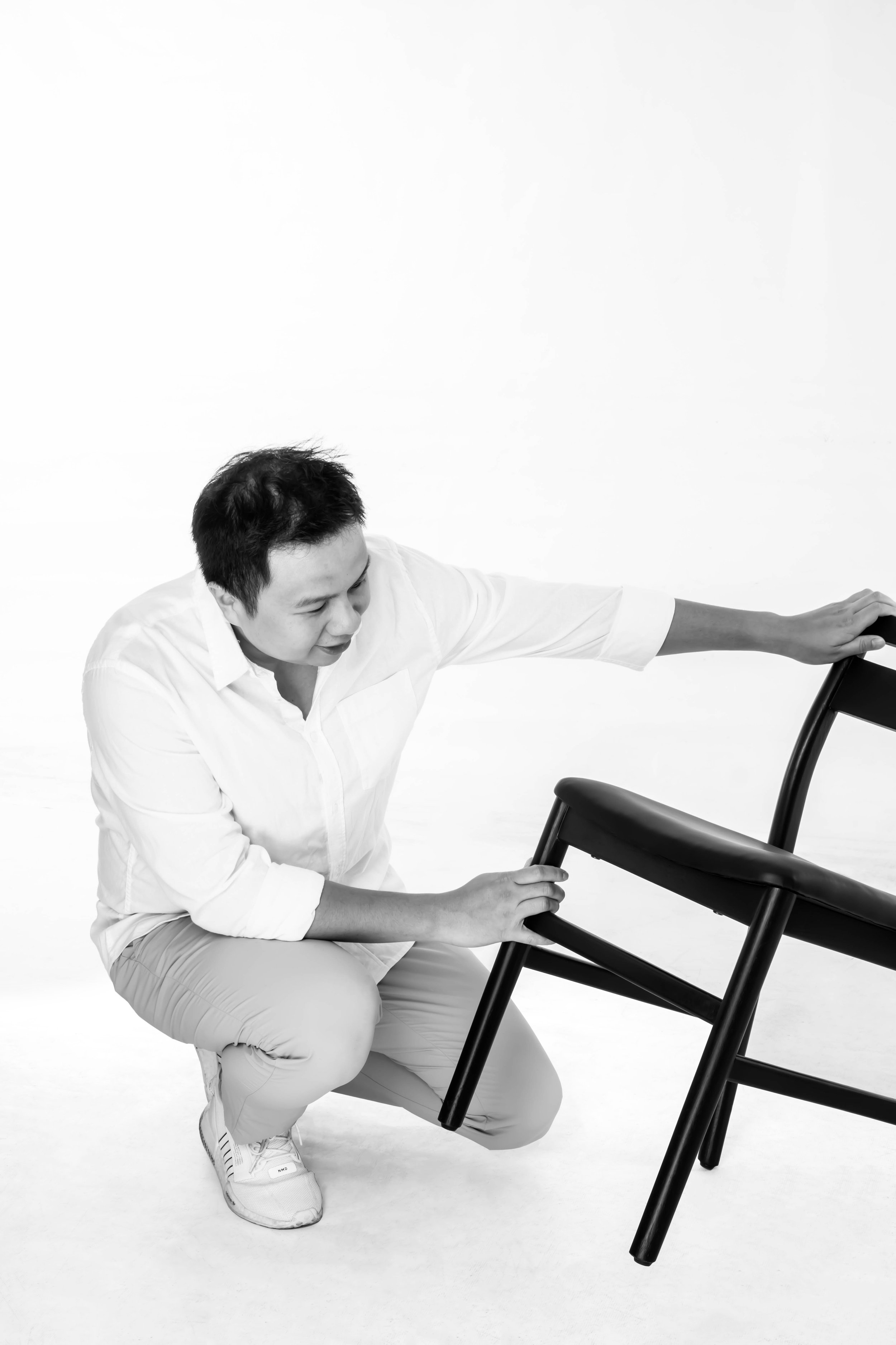 A person crouching and holding a black chair upside down.