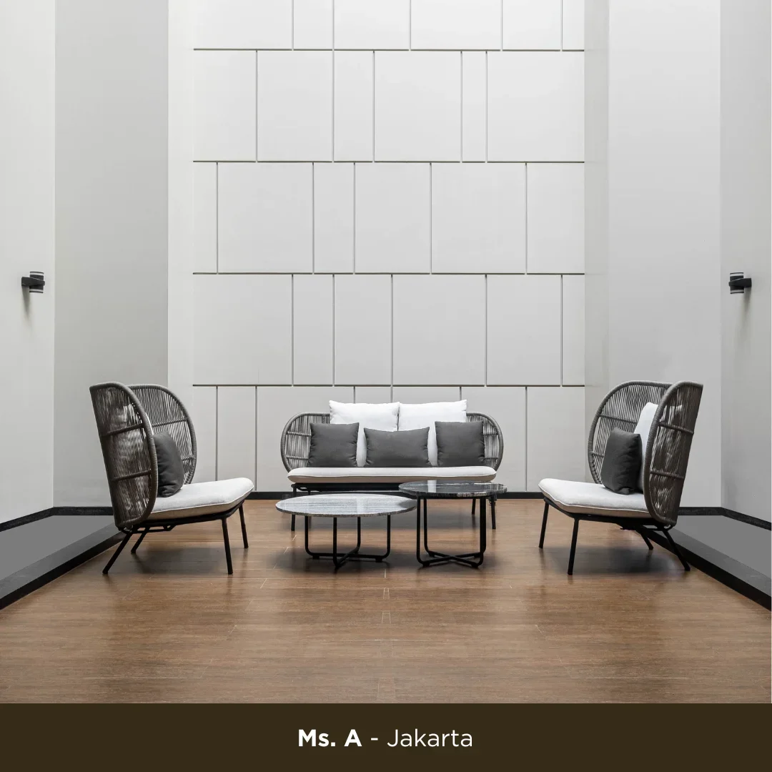 Modern sitting area with four black wicker chairs with white cushions and dark gray pillows, centered around two round coffee tables, situated in front of a textured white wall with geometric patterns, on a wooden floor, with minimalist wall sconces.