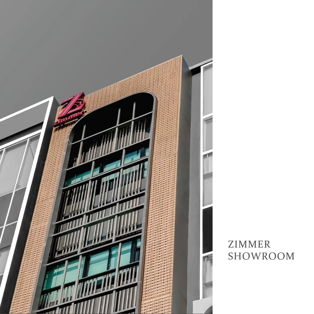 Exterior view of a modern building with a brown brick facade and glass windows, featuring a red Zimmer sign on the top left corner, indicating a showroom.