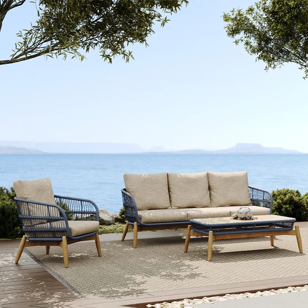 Outdoor patio furniture set with beige cushions and a rock on a coffee table, overlooking the ocean with trees around.